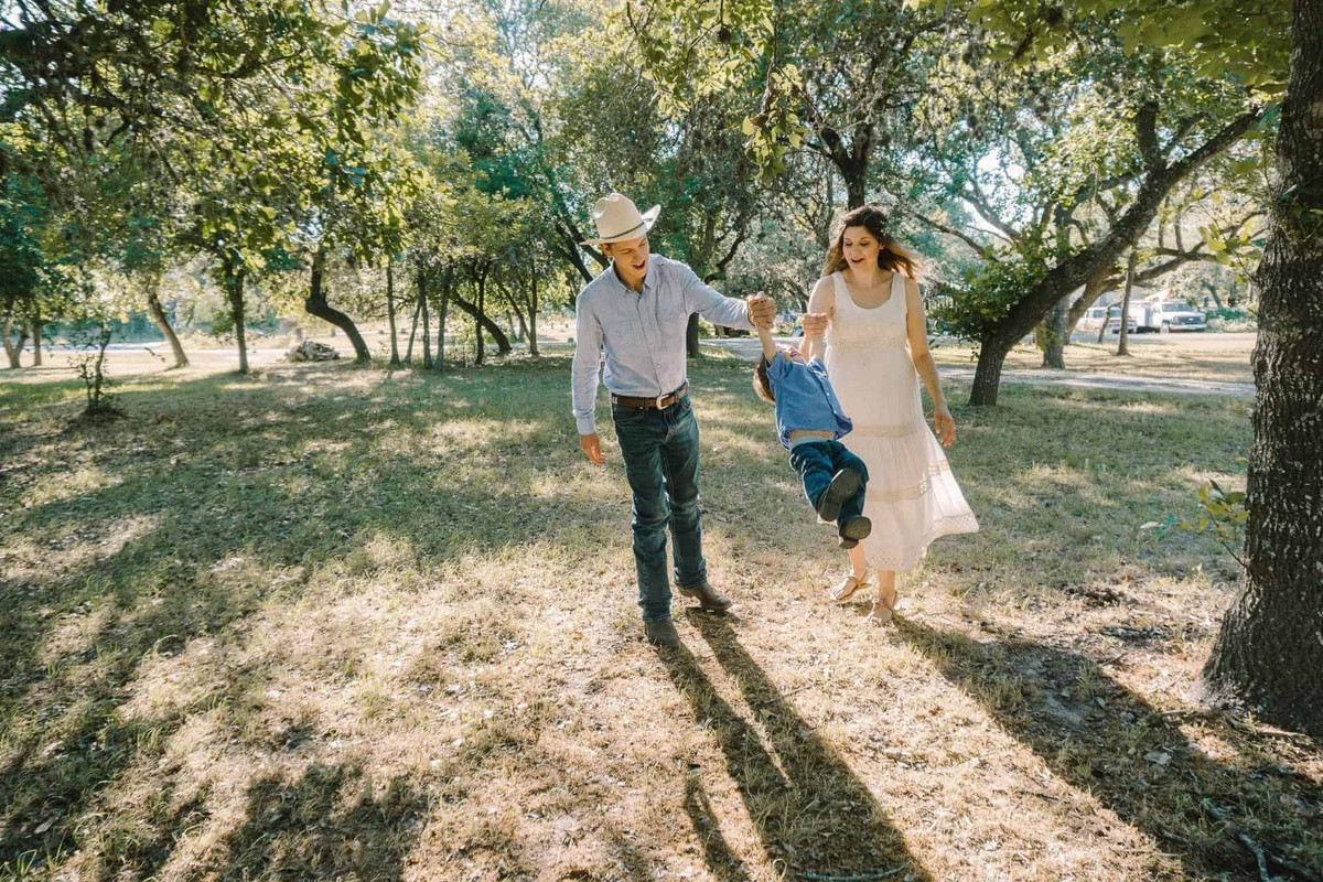 a man and woman swinging a small boy by the arms in play