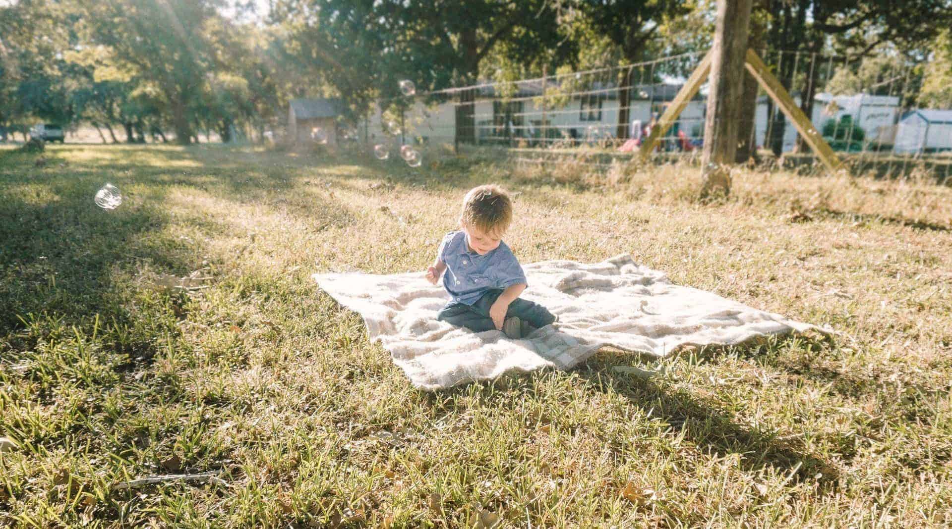 a child playing on a blanket in a field while bubbles float by