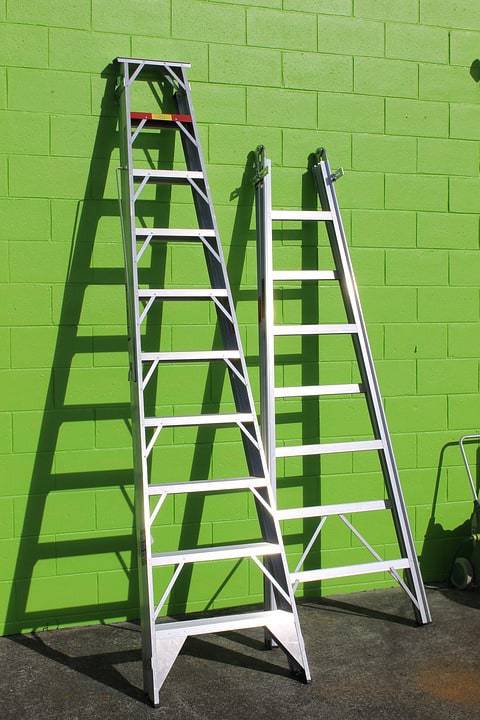 Two ladders leaning against a green, cement block wall