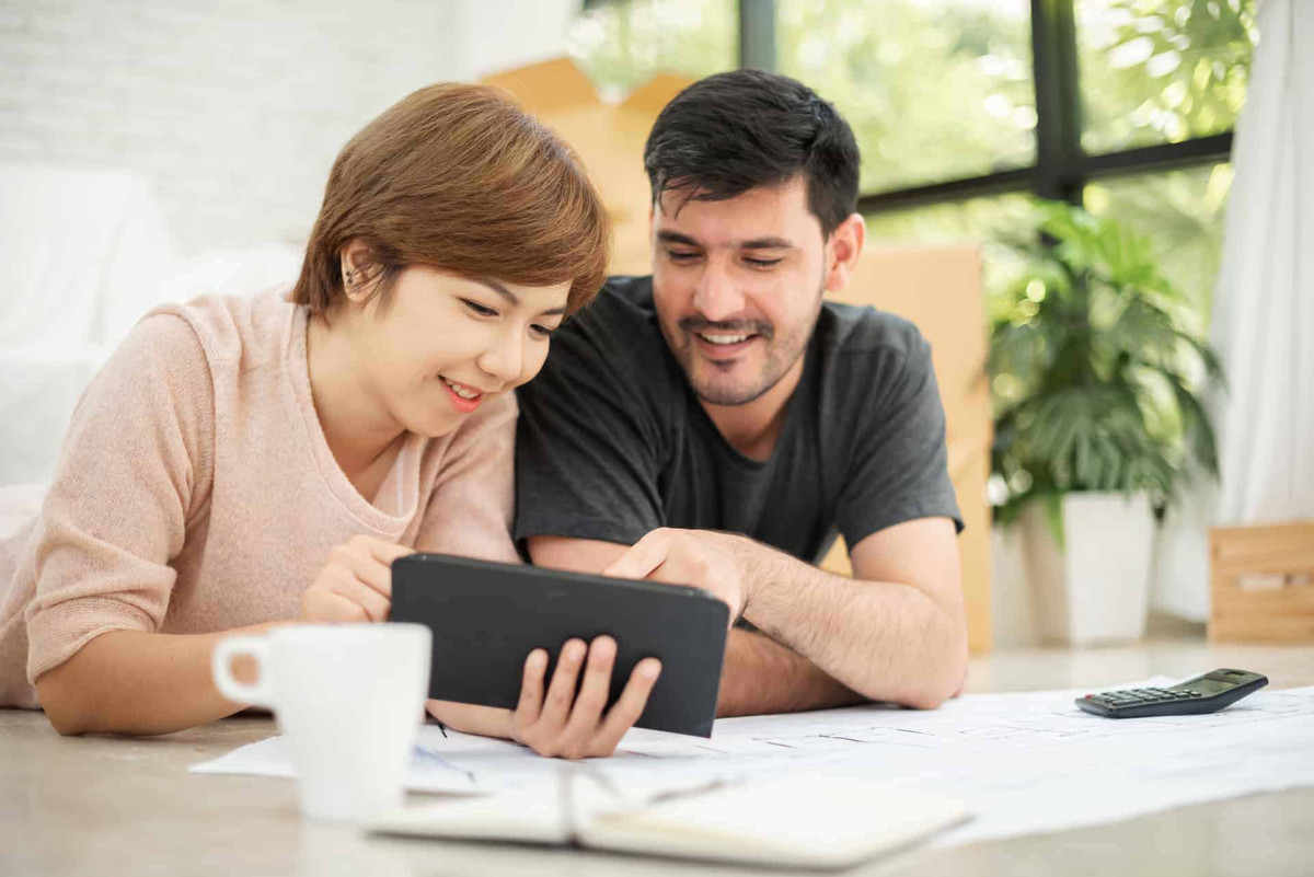 Happy young couple with digital tablet and blueprints planning their new house with smiling faces.