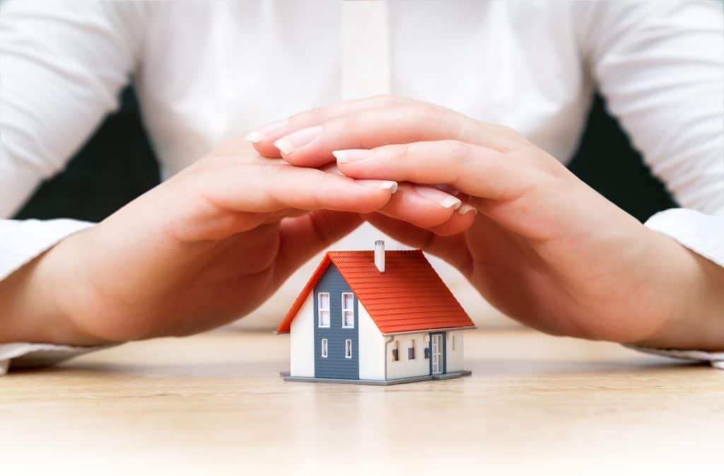 Woman covering a miniature house with her cupped hands