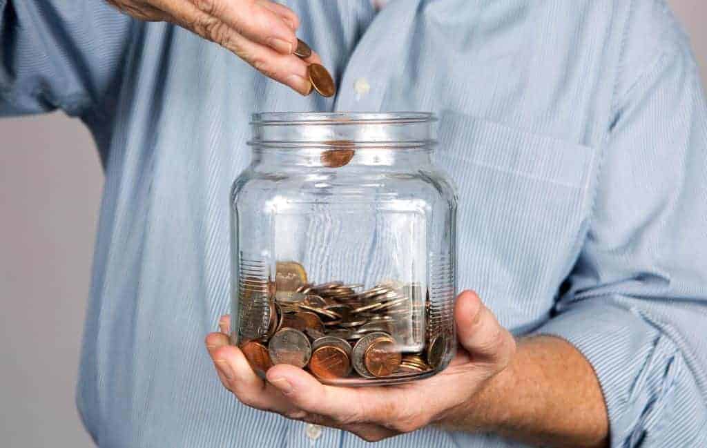 Man drops money into a glass jar for a savings account.