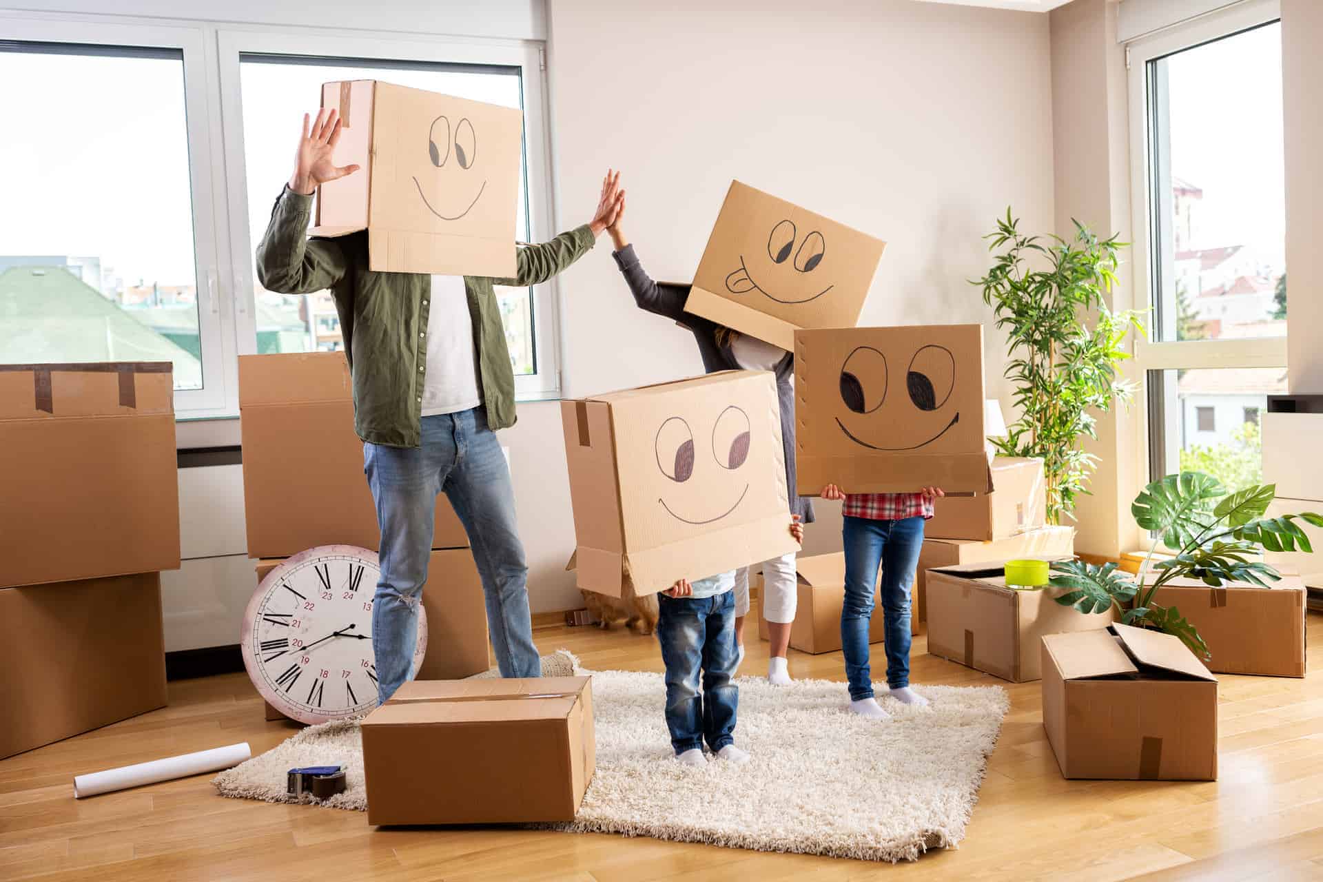 Family, surrounded by moving boxes, with moving boxes on their heads. The boxes on their heads have funny faces drawn on them.