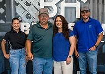4 adults posing in front of Braustin Homes Logo